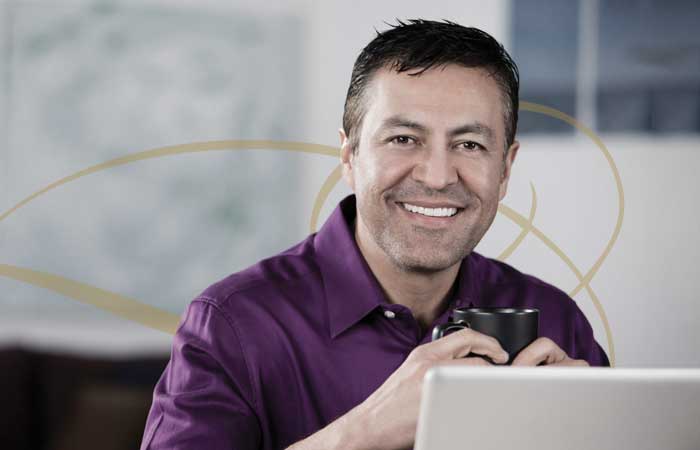 Man smiling in front of a computer holding a mug